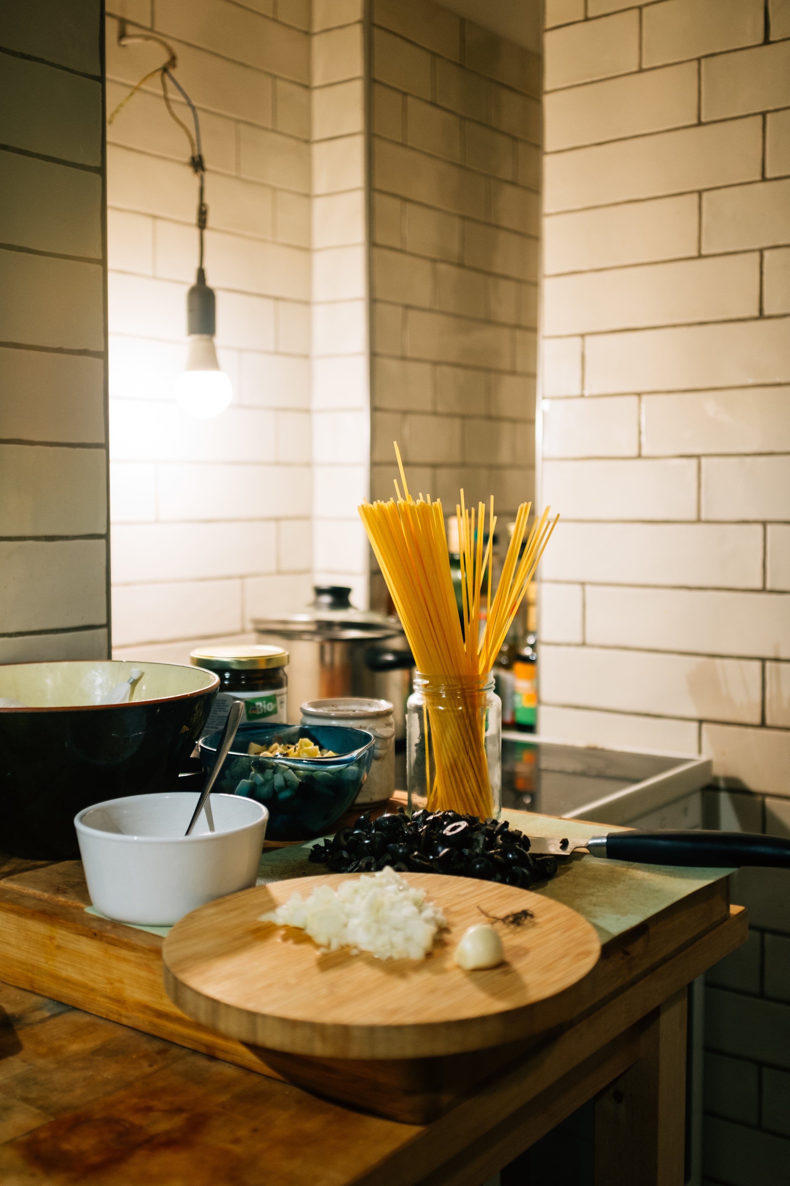 A simple kitchen with dried pasta, a small cutting board with garlic, and some mixing bowls